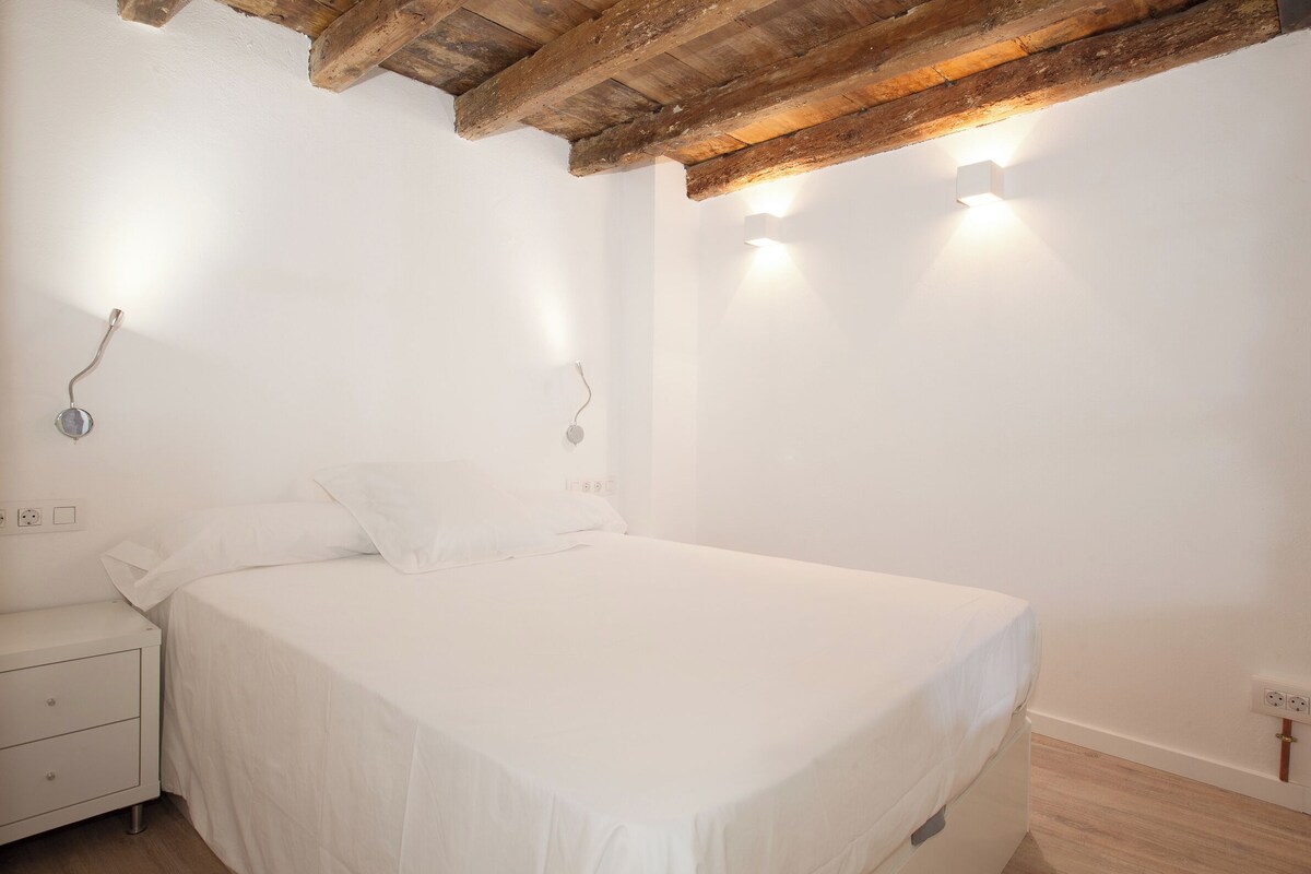 A bedroom with a bed, bedside table, and wall-mounted lights.