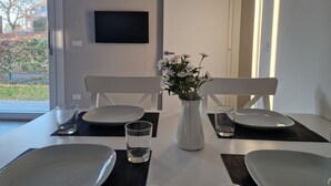 Ett matbord med stolar, en vas med blommor och en platt-TV på väggen.
