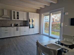 A modern kitchen with white cabinets, a built-in oven, and a large window. - Tiramisù included - By Flora (Treviso)