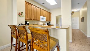 A kitchen with wooden cabinets, a microwave, and a bar area with bar stools. - Living the Disney Dream! | Lake View Luxury Condo (Orlando)