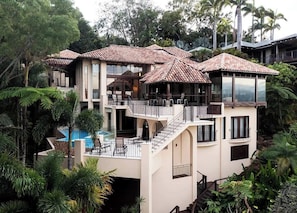 A multi-story house with a swimming pool, balconies, and lush greenery.