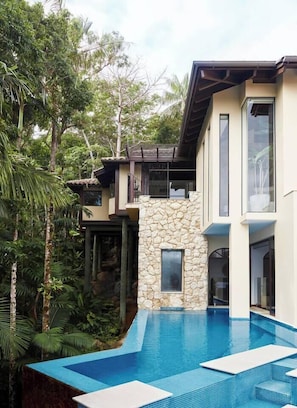 A modern house with a stone facade, a swimming pool, and lush greenery.