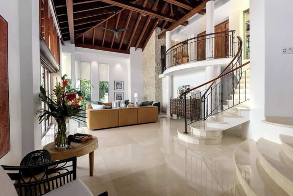 A spacious interior with a high ceiling, a central seating area, and a staircase leading to an upper level.