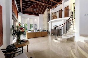 A spacious interior with a high ceiling, a central seating area, and a staircase leading to an upper level.