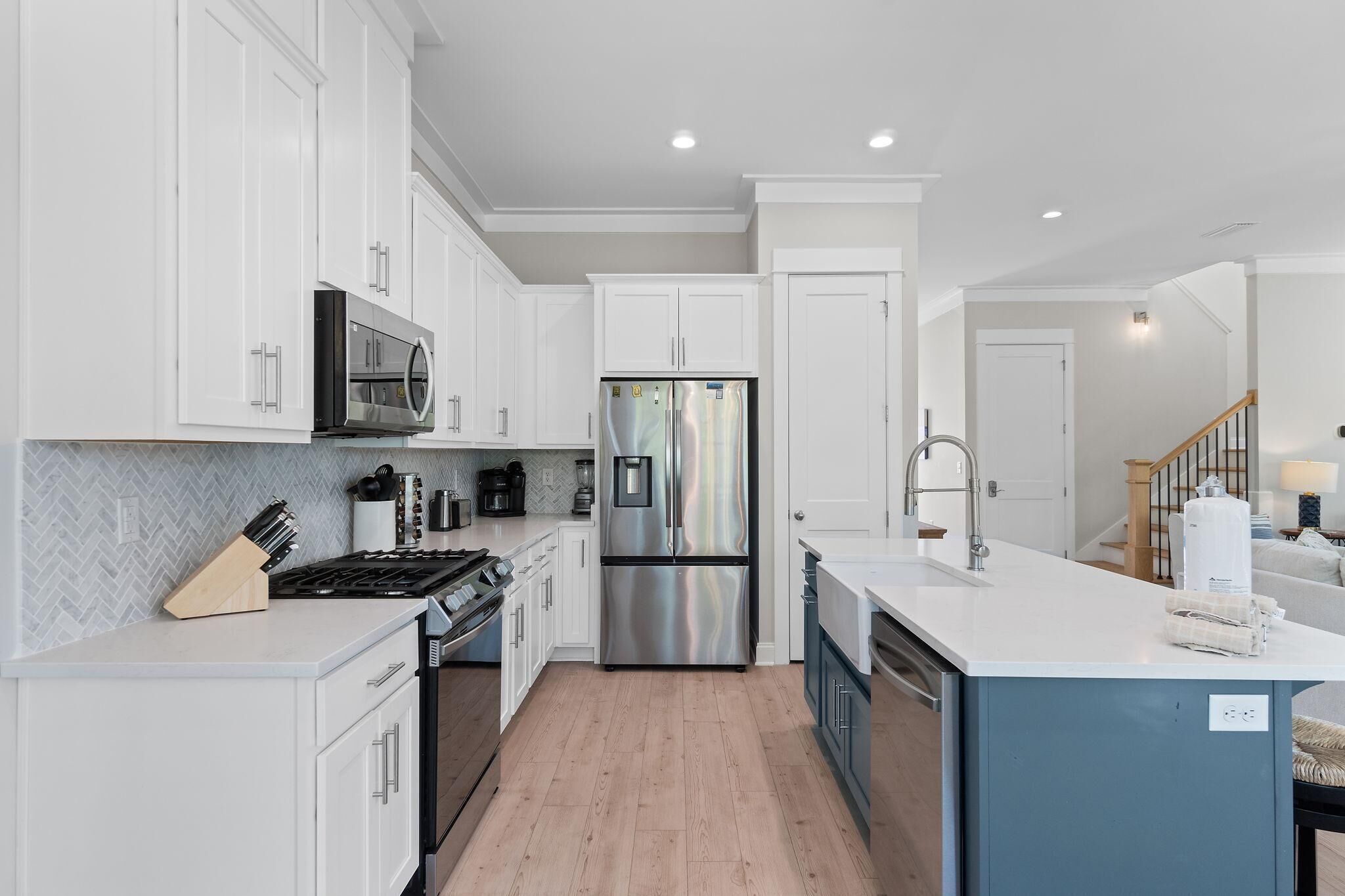 A modern kitchen with white cabinets, stainless steel appliances, and a wooden floor.