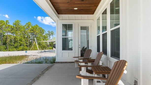 A covered outdoor seating area with wooden chairs and a table, overlooking a beach and trees. - Bama Breeze at Summer Salt (Orange Beach)