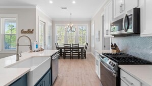 A modern kitchen with white cabinets, a stainless steel stove, and a dining area with a chandelier. - Bama Breeze at Summer Salt (Orange Beach)