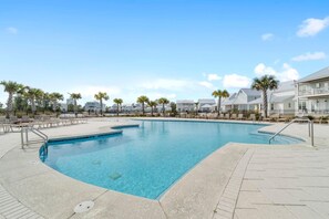 A swimming pool with a clear blue water, surrounded by lounge chairs and palm trees.