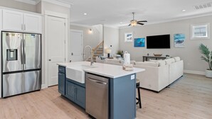 A modern kitchen with a central island, stainless steel appliances, and a dining area with a white sofa. - Bama Breeze at Summer Salt (Orange Beach)