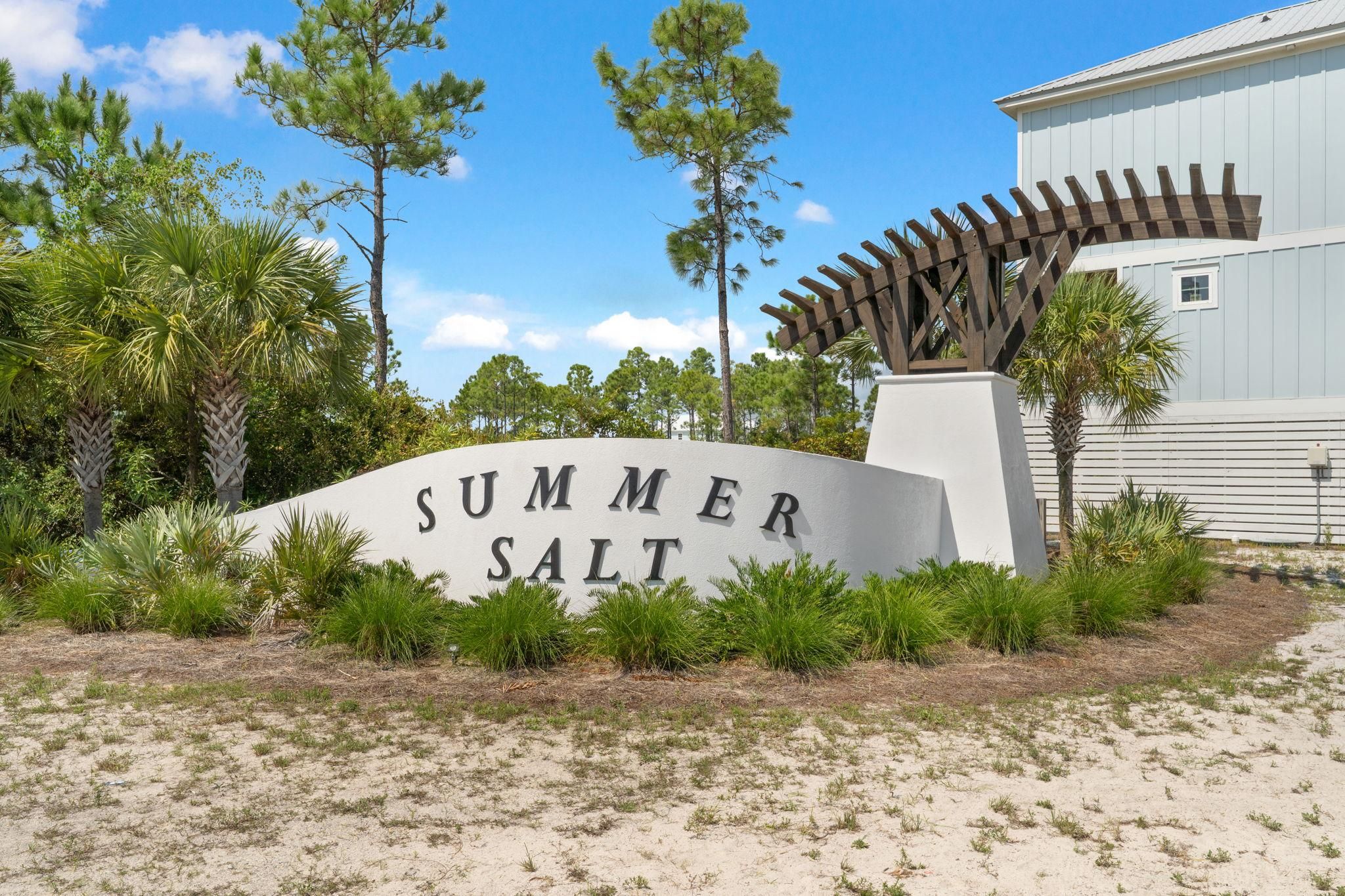 A sign with 'SUMMER SALT' written on it, surrounded by greenery and a wooden pergola structure.