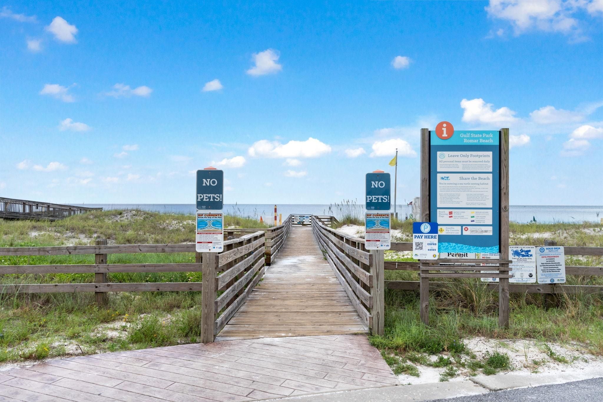 Een houten looppad dat naar een strand leidt, met borden waarop staat 'GEEN DIEREN' en informatieborden over Gulf State Park en strandregels.