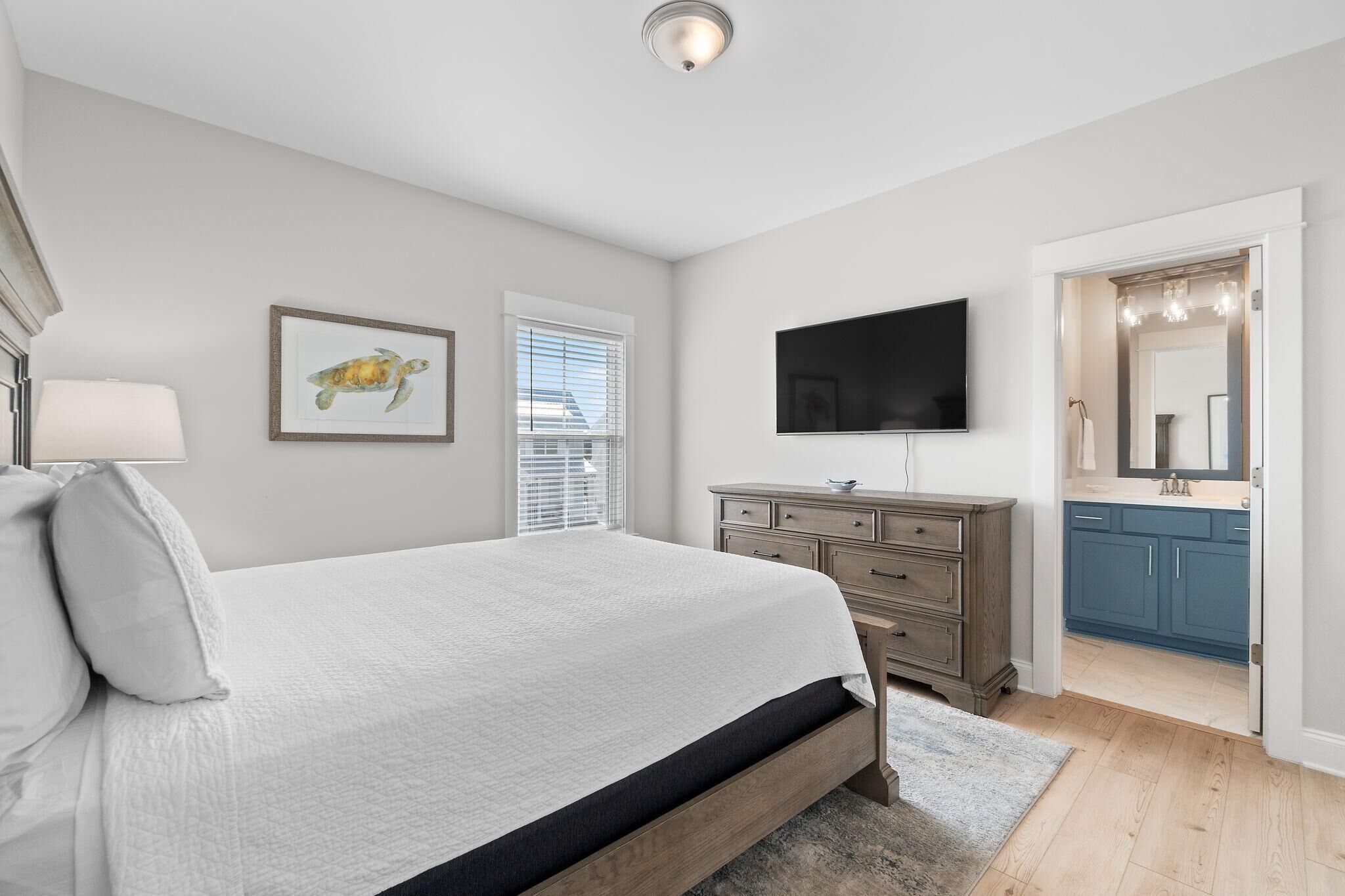 A bedroom with a bed, a dresser, a TV, and a bathroom visible through an open door.