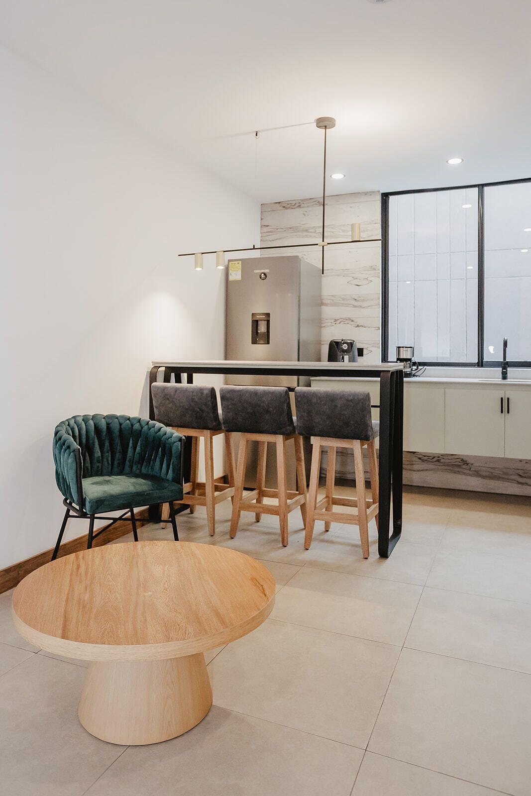 A modern kitchen with a bar area, a round wooden table, and a green upholstered chair.
