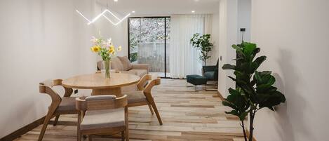 Un espace repas moderne avec une table ronde en bois et des chaises, un vase de fleurs et une grande fenêtre avec des rideaux.