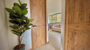 Un corridoio con porte in legno, una pianta in vaso e vista su un soggiorno con divano e finestra.