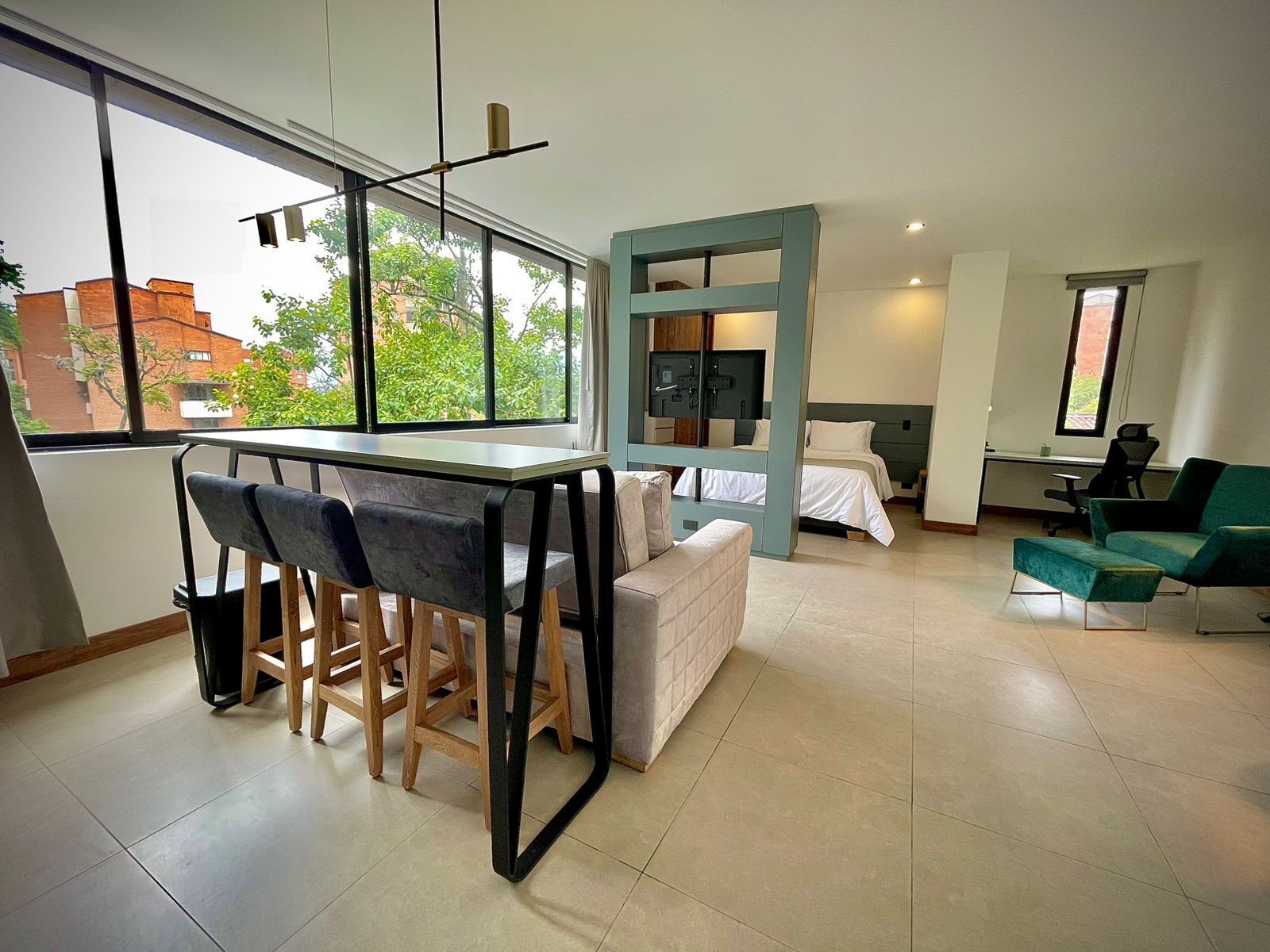 A modern, well-lit room with a dining area, a bed, a desk, and a green sofa.