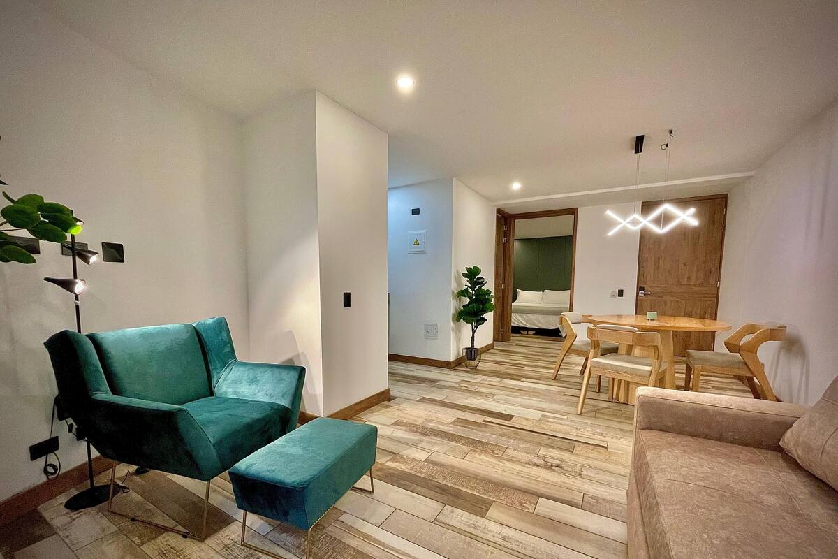 A modern living room with a teal sofa, a wooden dining table, and a wooden floor.