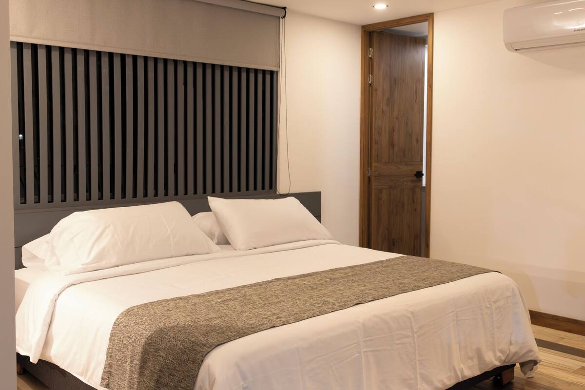 A modern bedroom with a large bed, wooden flooring, and a built-in headboard.