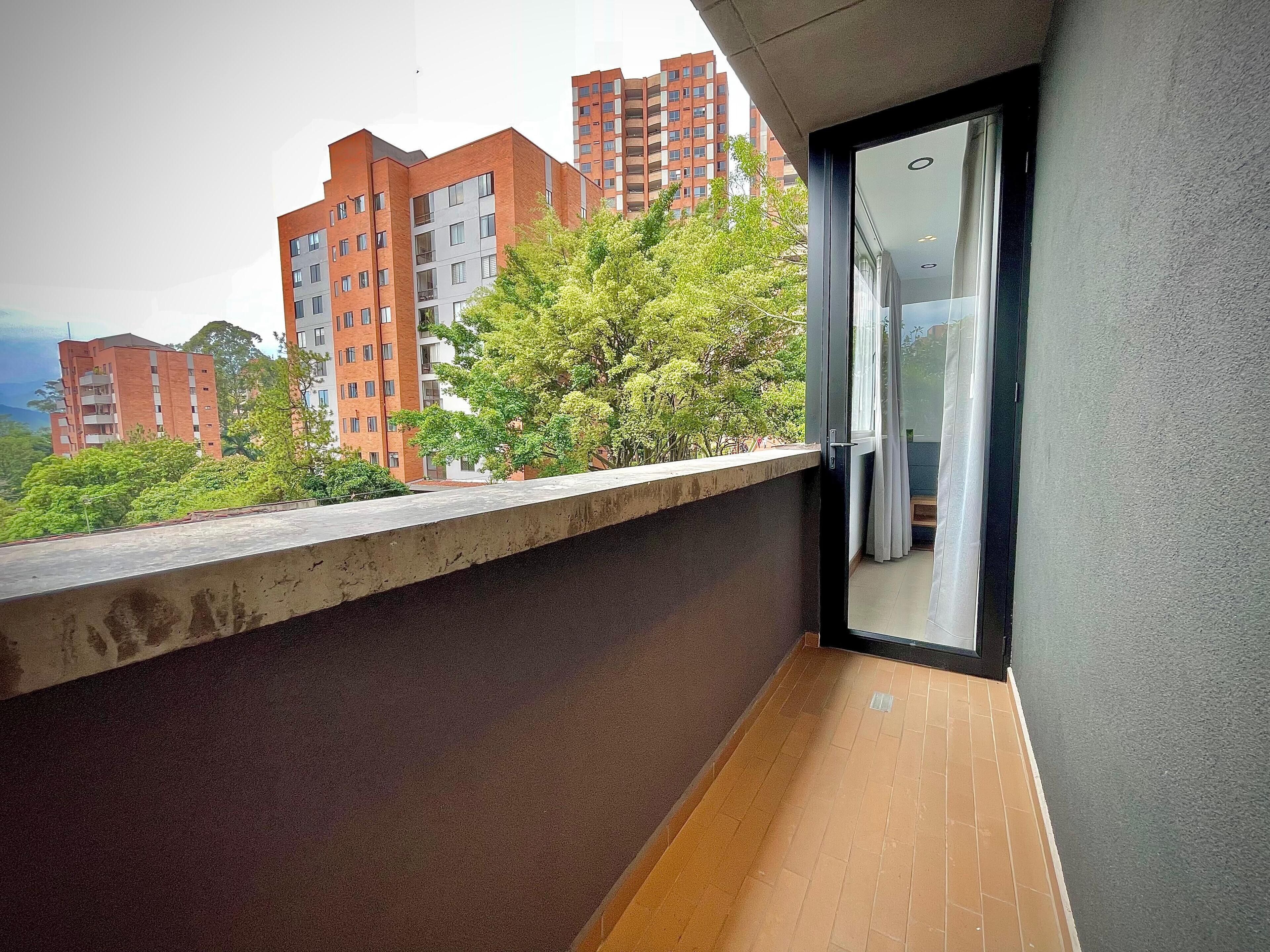 A balcony with a concrete ledge, a sliding glass door, and a view of adjacent high-rise buildings and greenery.
