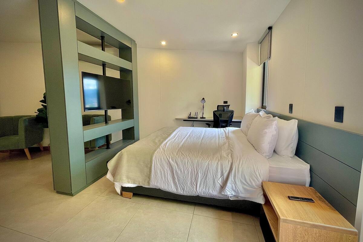 A modern hotel room with a large bed, a desk with a computer, and a TV.