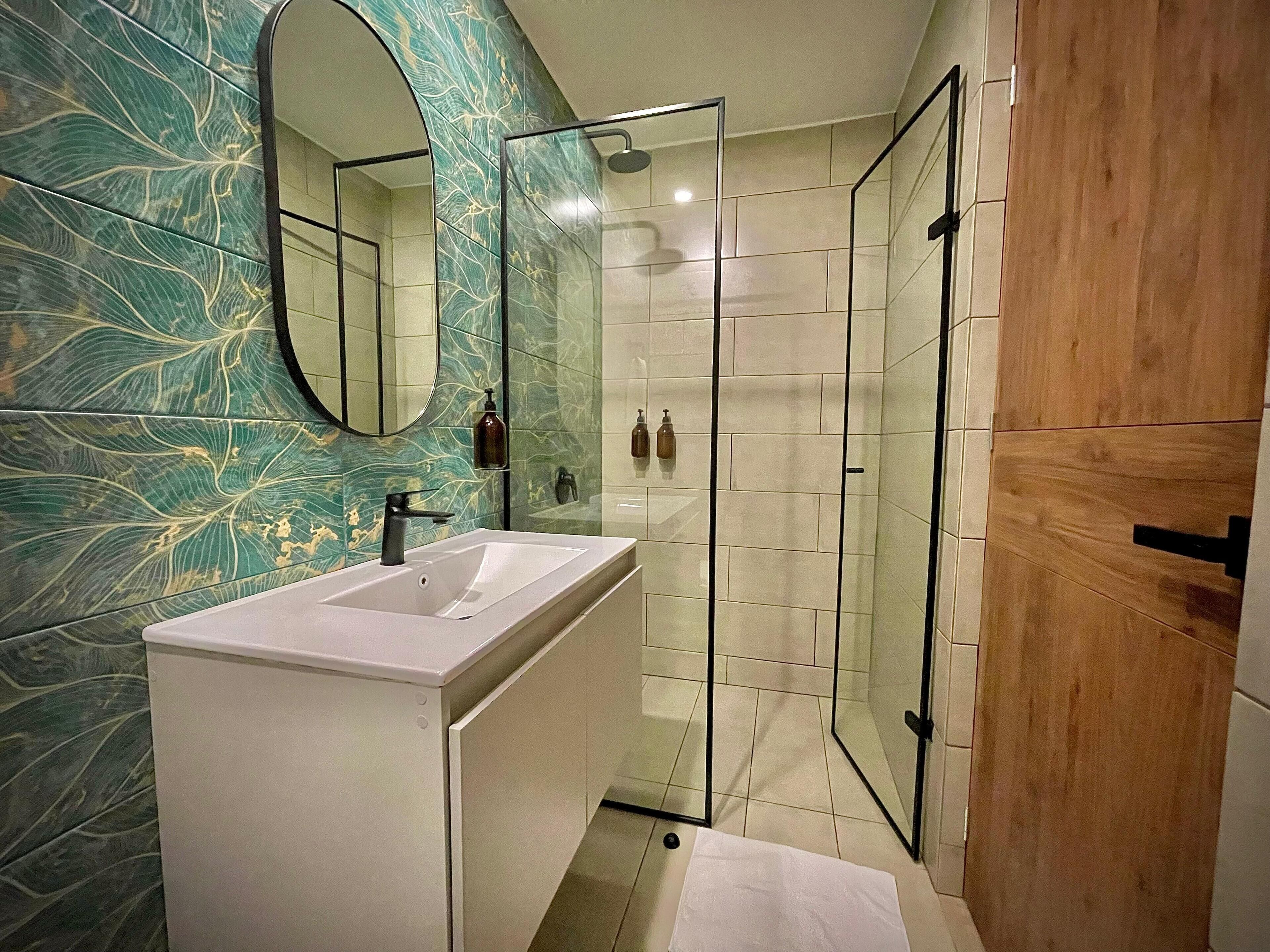 A bathroom with a white sink, a glass shower enclosure, and a wooden door.