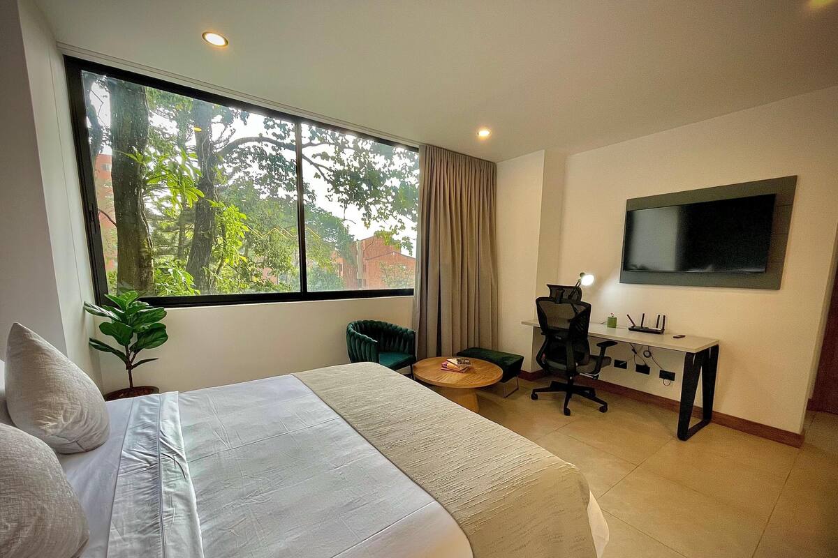 A hotel room with a large bed, a desk with a computer, a chair, and a TV.