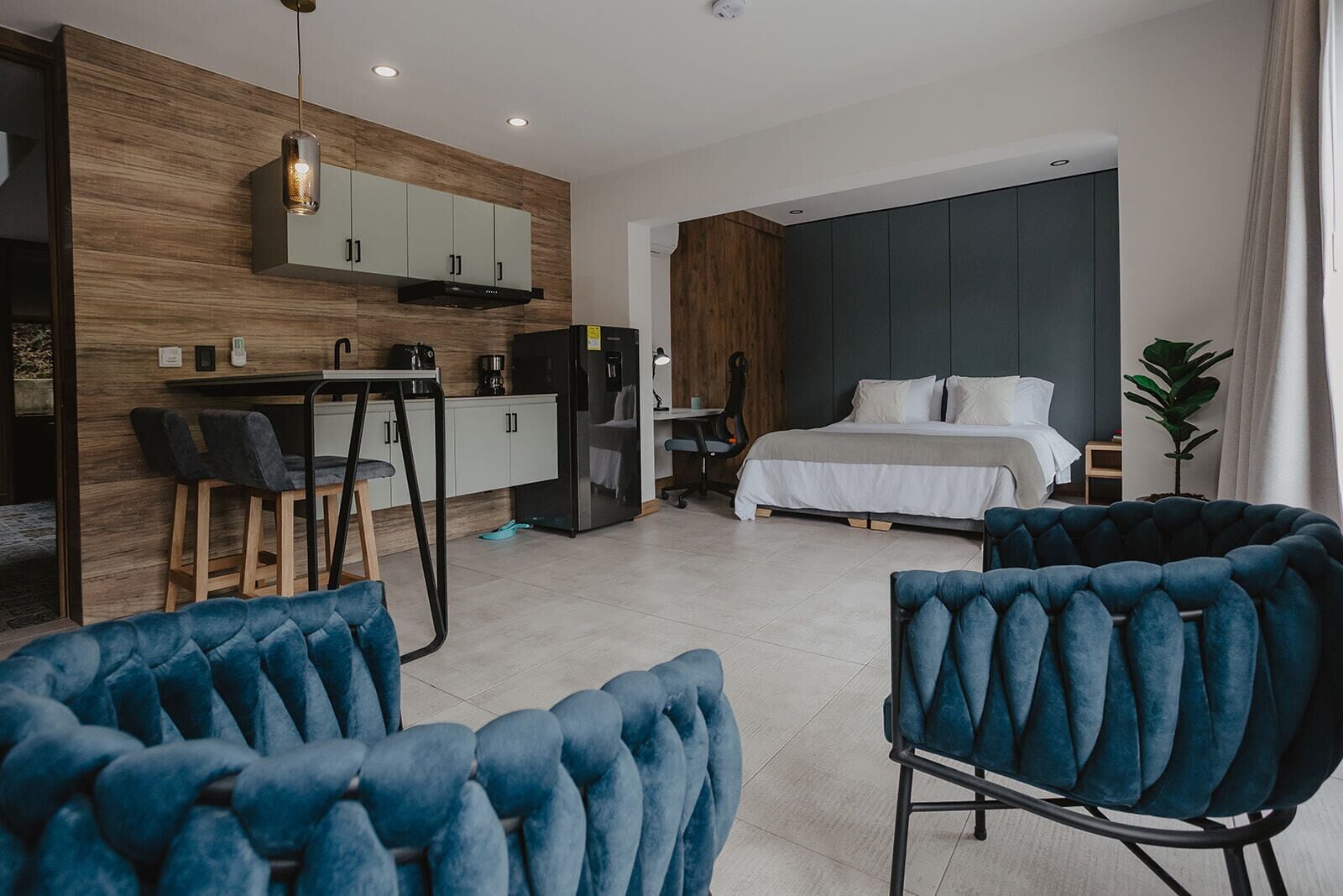 Quarto de hotel moderno com uma cama, uma escrivaninha com cadeira, um sofá e uma janela grande.