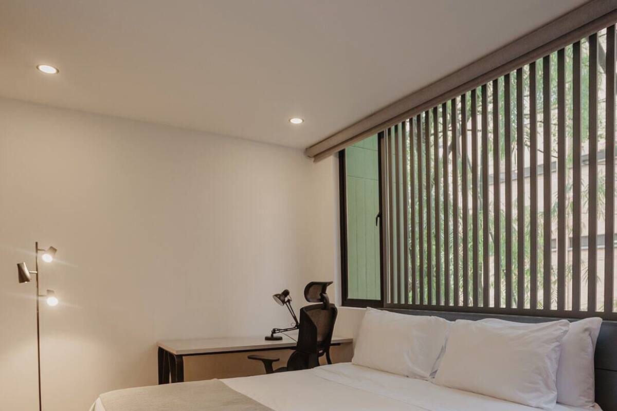 A modern bedroom with a large bed, a desk, and a floor lamp.
