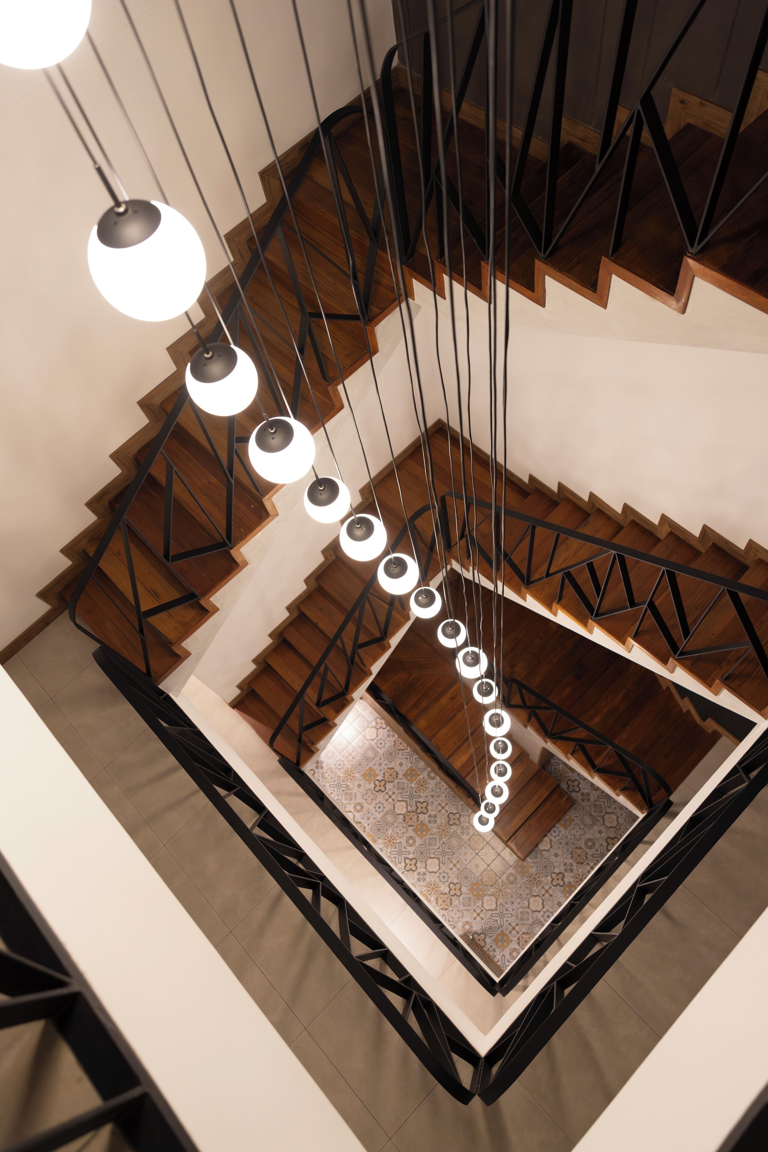 Eine moderne Treppe mit einem geometrischen Geländer und mehreren schwebenden, kugelförmigen Leuchten.