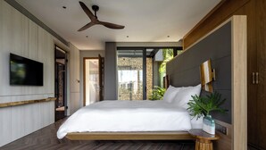 Ein modernes Schlafzimmer mit einem großen Bett, einem Deckenventilator, einem Fernseher und Blick ins Freie.