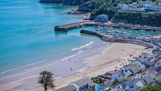 A coastal town with a sandy beach, a marina, and buildings along the shore.