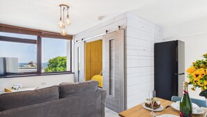 A modern living room with a sofa, dining table, and a view of the sea through large windows.