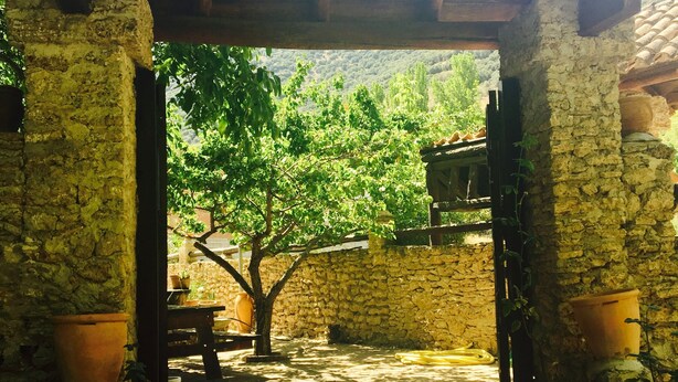 A rustic stone archway leading to a courtyard with a tiled roof, stone walls, and potted plants.