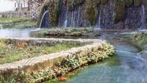 A natural water feature with multiple waterfalls, surrounded by stone walls and vegetation.