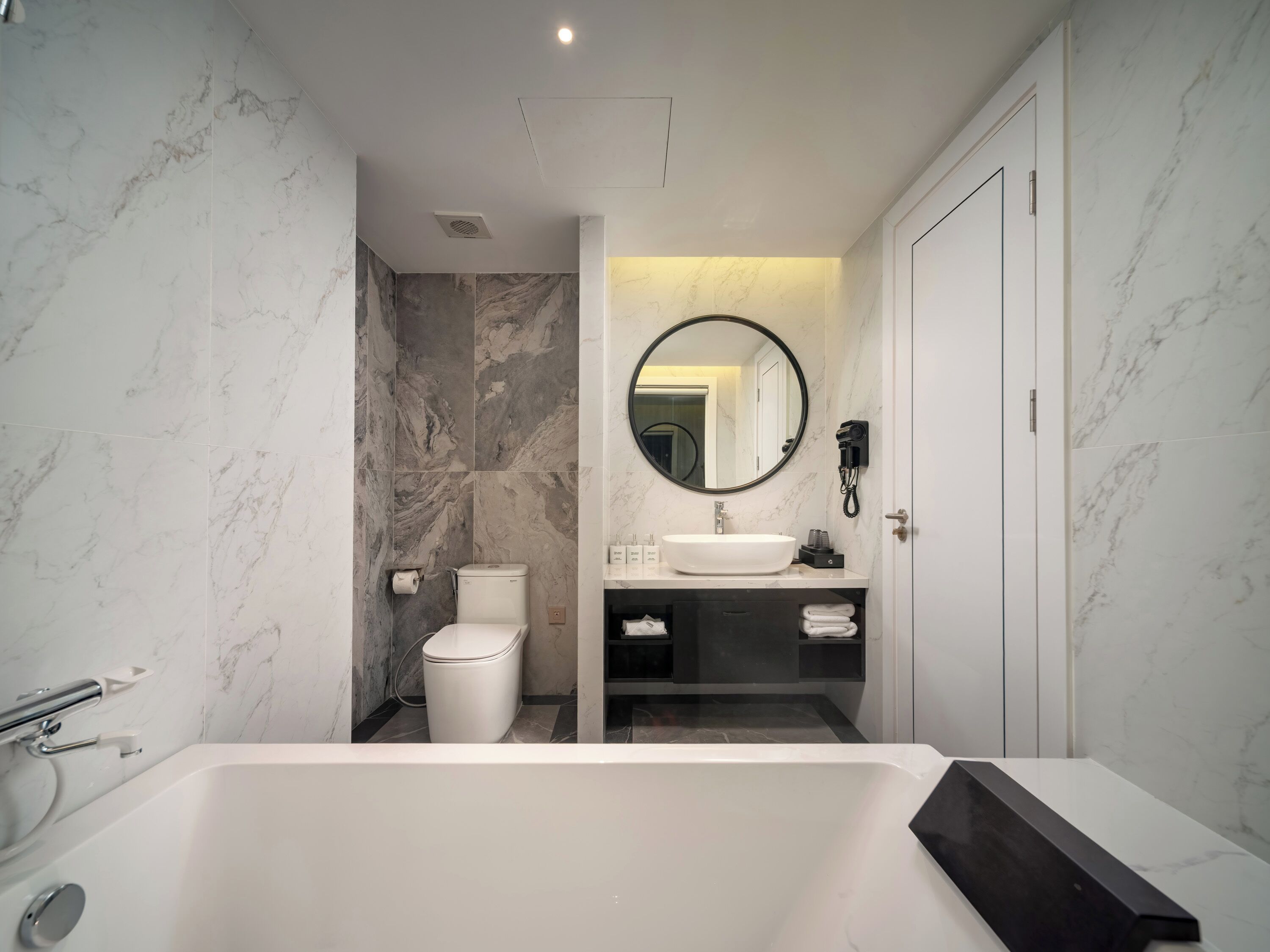 A modern bathroom with a white bathtub, a toilet, a sink, and a mirror.