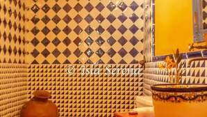 Une salle de bain avec un mur recouvert de carreaux à motifs, des toilettes, un lavabo agrémenté d’un récipient décoratif et un miroir.