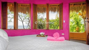 Une chambre avec un grand lit, des murs roses et des fenêtres donnant sur un paysage tropical.