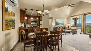 A spacious living area with a dining table set for four, a sofa, and a large window offering a view.