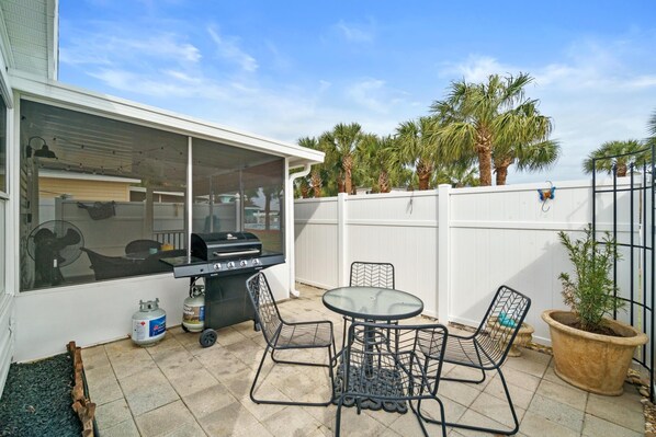 A patio with a grill, outdoor table, chairs, and a potted plant.