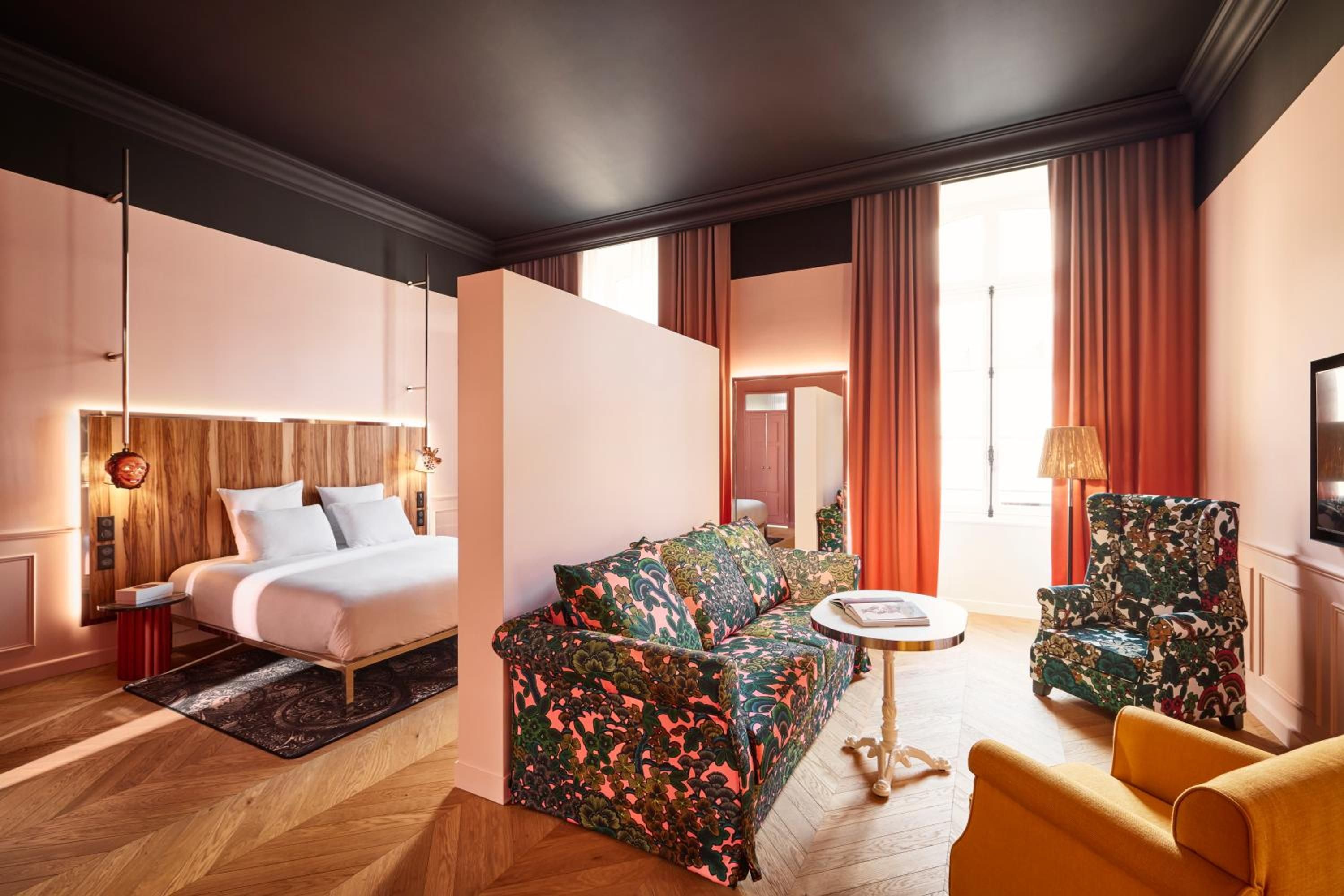 A hotel room with a bed, a sofa, a chair, a small table, and a television.