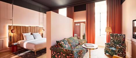 A hotel room with a bed, a sofa, a chair, a small table, and a television.