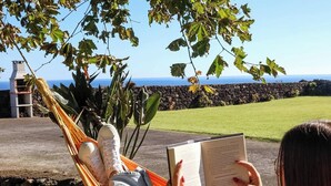 Une personne se détend dans un hamac, un livre à la main, et profite de la vue sur une pelouse et un mur de pierre.