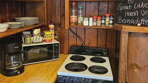 Een keuken met een fornuis, koffiezetapparaat en planken met keukengerei en kruiden.