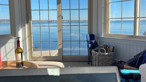 Et værelse med stort vindue med udsigt over vand, en fletstol, en vinflaske og et skilt med teksten "relax".