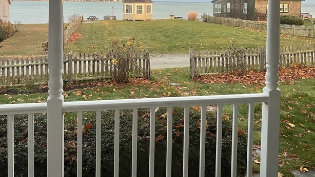 A coastal view from a porch with a white railing, overlooking a grassy area with a small gazebo and a larger house. - World Cup Ocean retreat 40 minute drive from Boston Stadium - Gillette  (Fairhaven)
