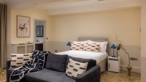 A hotel room with a bed, a sofa, a small table, a lamp, and a wall-mounted mirror. - Newly refurbished, Superior studio Lower Ground (London)