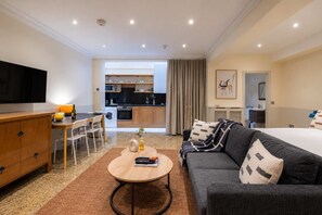 Ein modernes Hotelzimmer mit Sofa, Essbereich, Küche und Fernseher.
