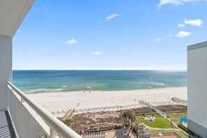 A beach view from a balcony with a clear sky, a sandy beach, and a few people walking. - Palacio 705 (Pensacola)