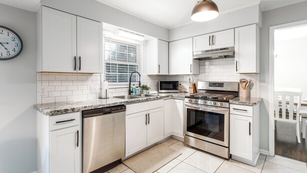 A modern kitchen with white cabinets, stainless steel appliances, a clock, and a window.