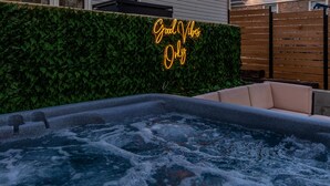 A hot tub with a neon sign reading "Good Vibes Only" in a backyard setting.